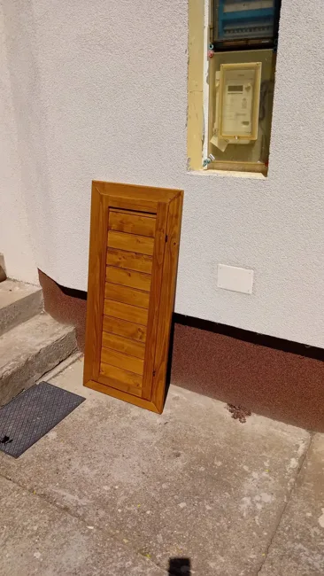 Barna fa burkolóajtó a falba épített villanyóraszekrény előtt.