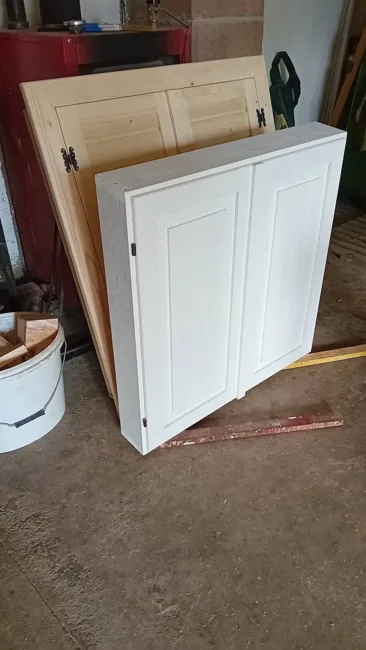 Fehér, kétajtós kazettás villanyóraszekrény-ajtó a munkapadon.